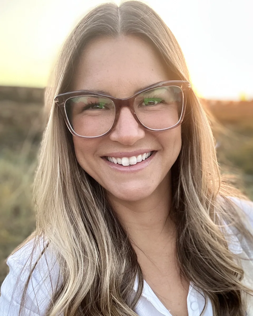 Jackie Flietstra smiling, in glasses and a white shirt, in warm evening light.